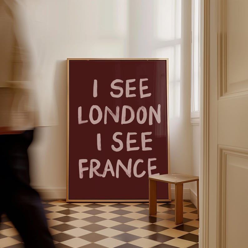 May include: A framed burgundy artwork with the text "I SEE LONDON I SEE FRANCE" in white. The artwork is in a room with a small wooden stool and a black and white checkered floor.