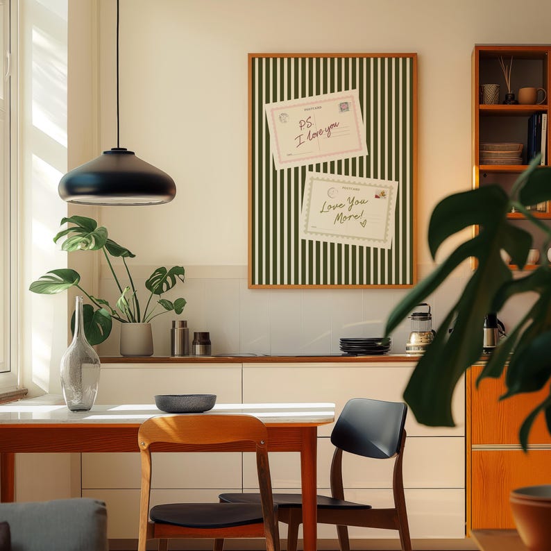 May include: A modern interior scene featuring a dining table with two chairs, a decorative framed board with postcards, and a hanging black pendant light. The board has a green and white striped pattern. The postcards read "PS I love you" and "Love You More!"