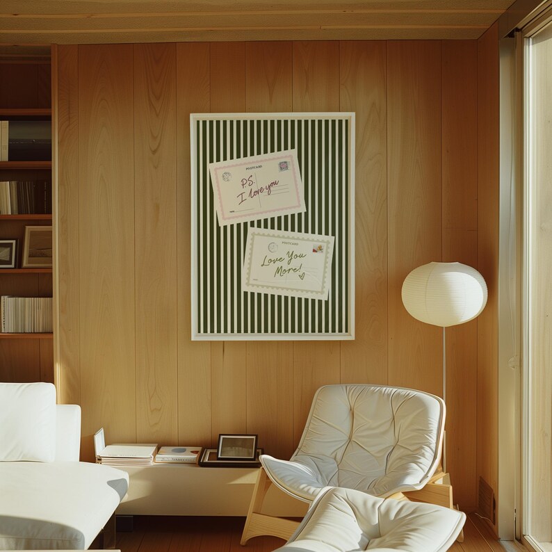 May include: A framed artwork with a white border features a green and white striped background. Two postcards are attached, one with "PS I love you" and the other with "Love You More!". The artwork hangs on a wood-paneled wall.