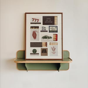 May include: A framed art piece featuring various matchbox designs with text like "777", "The End", and "Lucky You". The artwork is displayed on a green and wood-toned shelf, creating a vintage aesthetic.