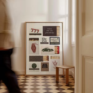 May include: A framed art piece featuring various matchbox designs. The designs include text like "777", "These are the good old days", "The End", and "Lucky are we". The artwork is displayed in a room with a checkered floor and a small wooden table.