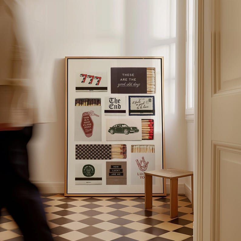 May include: A framed art piece featuring various matchbox designs. The designs include text like "777", "These are the good old days", "The End", and "Lucky are we". The artwork is displayed in a room with a checkered floor and a small wooden table.