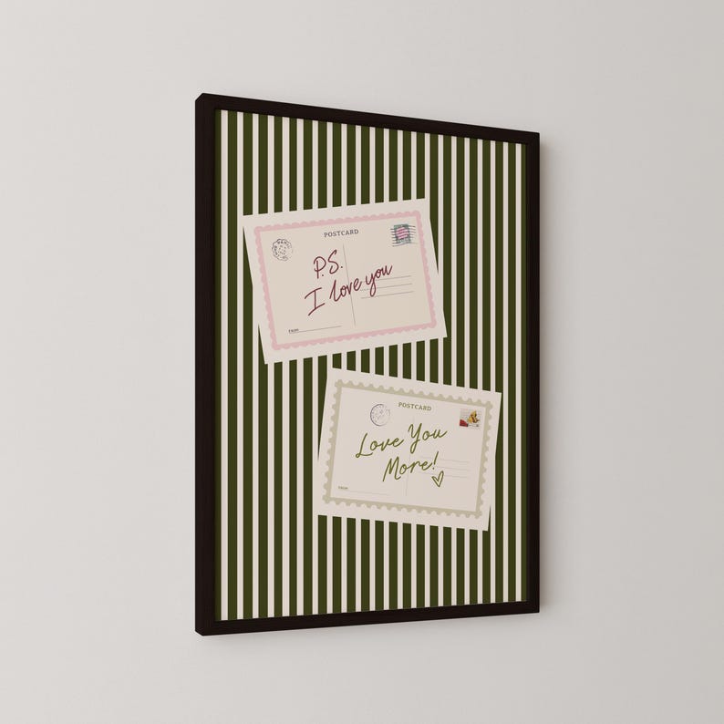 May include: A framed wall art piece featuring a dark olive green and white vertical striped background. Two rectangular postcards are displayed on the stripes. The top postcard has a pink border and the text P.S. I love you. The bottom postcard has a scalloped border and the text Love You More! with a small heart.