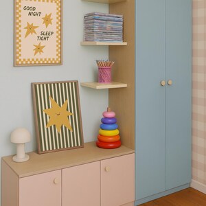 Puede incluir: Interior de habitaci&oacute;n infantil con armario azul claro, mueble de almacenamiento rosa y estanter&iacute;as de madera. Las estanter&iacute;as contienen un tarro morado, libros y l&aacute;pices. Las obras de arte incluyen un estampado enmarcado con el texto "GOOD NIGHT SLEEP TIGHT" y un dise&ntilde;o de estrella.