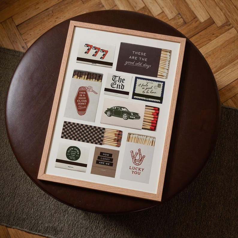 May include: A framed art print featuring various matchbox designs. The designs include text like "777", "The End", "Lucky You", and "This is a High Class Joint". The color palette includes red, white, black, and brown.