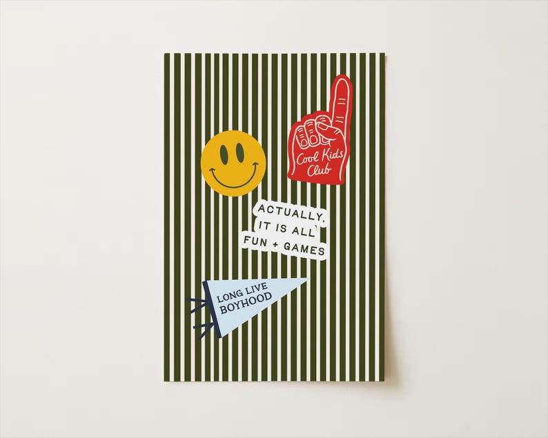 May include: A decorative card with a green and white striped background. The card features a yellow smiley face, a red foam finger with "Cool Kids Club" text, a white sticker with "ACTUALLY, IT IS ALL FUN + GAMES" text, and a blue pennant with "LONG LIVE BOYHOOD" text.