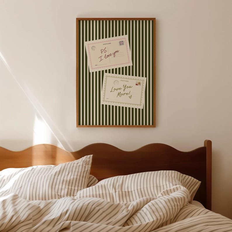 May include: A framed wall art piece with a green and white striped background. Two postcards are attached to the art, one reading "P.S. I love you" and the other "Love You More!" The frame is brown and the art is hanging above a bed.