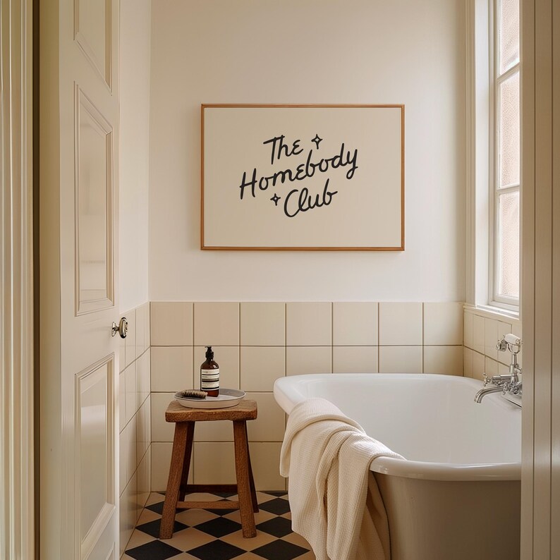 May include: A bathroom scene featuring a white bathtub, a wooden stool, and a framed sign that reads "The Homebody Club." The room has a neutral color palette with black and white checkered flooring and a window.