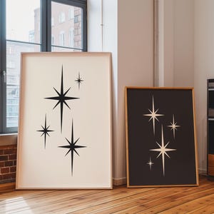 May include: Two framed art prints featuring mid-century modern starburst designs. One print has black stars on a cream background, the other has cream stars on a black background. Both are in light wood frames.