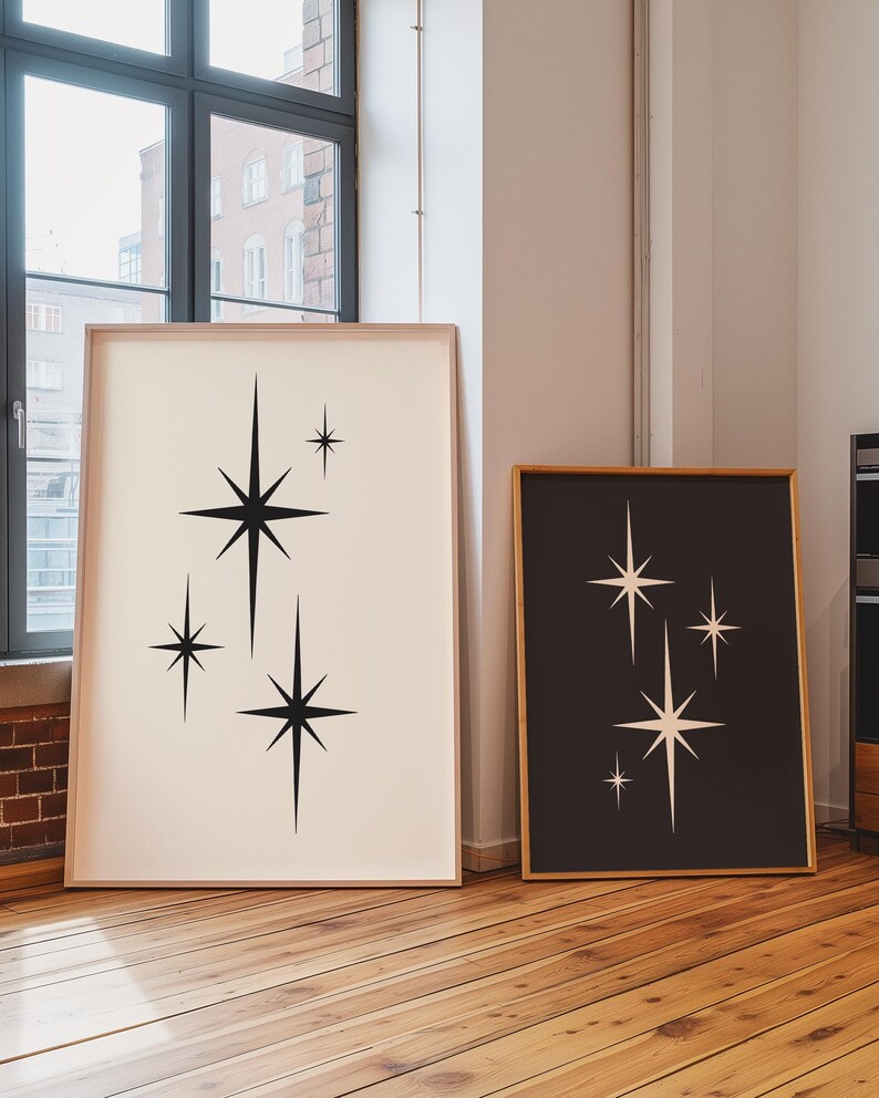 May include: Two framed art prints featuring mid-century modern starburst designs. One print has black stars on a cream background, the other has cream stars on a black background. Both are in light wood frames.