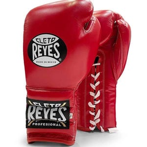 Op de afbeelding: Paar rode leren bokshandschoenen met witte veters. De handschoenen hebben het "CLETO REYES" logo in zwart en wit en de tekst "HECHO EN MEXICO". De handschoenen zijn gelabeld met "PROFESIONAL".