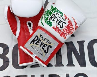 May include: Pair of red and white boxing gloves with the brand name "CLETD REYES" visible. The gloves have a Mexican flag design and the text "HECHO EN MEXICO PROFESIONAL". The background includes the text "BOXING STUDIO" and a phone number.