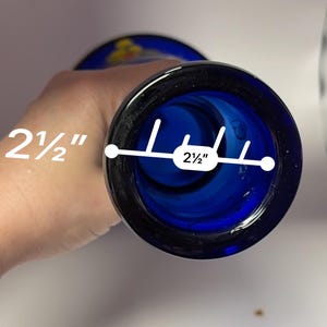 May include: A cobalt blue glass vase with a 2.5-inch opening. The vase has a dark blue rim and a slightly flared shape. The interior is a deep blue color, and the vase appears to be handmade.