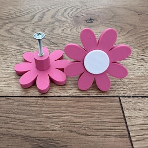 Op de afbeelding: Twee roze bloemvormige kastknoppen met een wit centrum. Eén knop heeft een zilveren schroef.