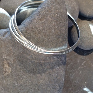 May include: Three silver bangles stacked on top of each other, resting on a grey rock.