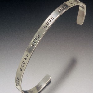 May include: A silver bangle bracelet with the inscription "This woman with love and light".