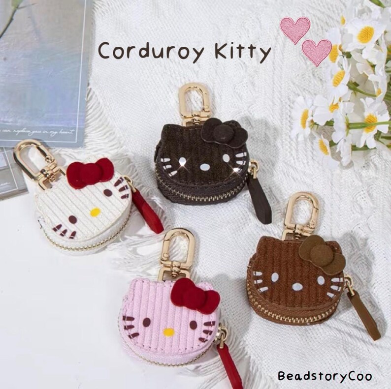 May include: Four corduroy Kitty-shaped coin purses in white, brown, pink, and dark brown. Each purse has a red bow, gold zipper, and a matching wrist strap. The text "Corduroy Kitty" is at the top.
