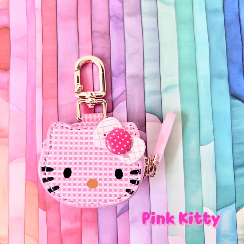 May include: A pink Hello Kitty keychain with a gold-colored clasp and a pink strap. The keychain features a pink and white checkered pattern, a white bow with pink polka dots, and the text "Pink Kitty".