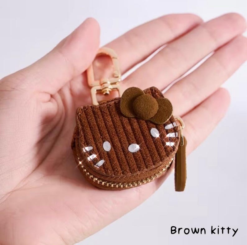 May include: Brown corduroy kitty-shaped coin purse with a gold zipper and clasp. The purse features a brown bow and white accents. The text "Brown kitty" is visible at the bottom of the image.