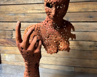 May include: A terracotta sculpture of a human torso with a single arm raised. The sculpture is made of many small, round pieces of clay, creating a textured surface.