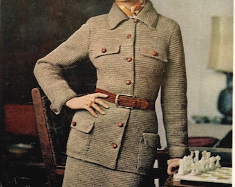 May include: A woman wearing a brown knitted jacket and skirt with a brown leather belt. She is wearing a brown hat with a black band and has a chessboard in front of her.