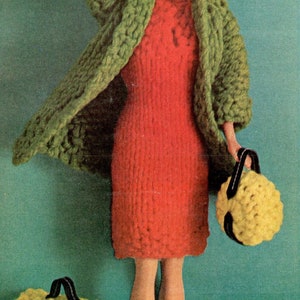 May include: A doll wearing a green crocheted cardigan, a red crocheted dress, and holding three yellow crocheted bags.