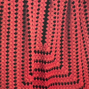 May include: A red and black crocheted throw blanket with a geometric pattern. The blanket is folded and draped over a wooden chair.