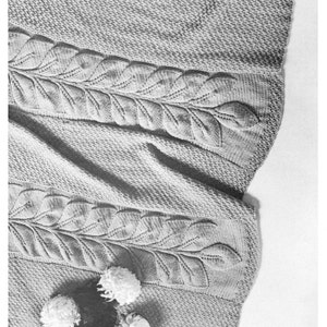 May include: A gray knitted blanket with a leaf pattern. The blanket is folded and draped over a white surface with white flowers.