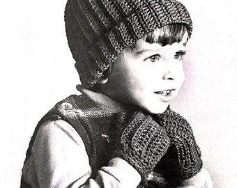 May include: A black and white photo of a young child wearing a knitted hat and mittens. The hat has a pom-pom on top and the mittens are folded over the child's hands.