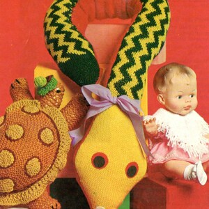 May include: A knitted yellow snake toy with green and yellow zig-zag pattern on the neck, a brown turtle toy with yellow spots, and a doll wearing a pink dress and white shawl.