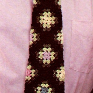 May include: A crocheted tie with a pattern of colorful squares. The tie is made with brown, yellow, pink, and blue yarn.