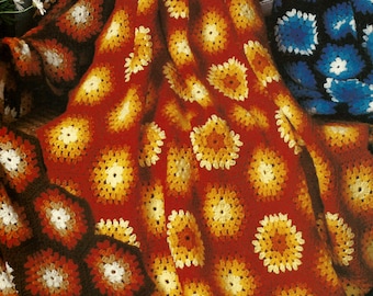 May include: A handmade crochet blanket featuring a repeating floral pattern in shades of red, orange, yellow, and white. The blanket has a textured appearance and is folded over a surface. The overall theme is home decor.
