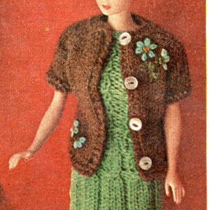 Puede incluir: Mu&ntilde;eca vestida con un atuendo hecho a mano. El conjunto incluye un vestido de punto verde y una chaqueta bolero marr&oacute;n con botones blancos y adornos florales. La mu&ntilde;eca tiene cabello rubio, sobre un fondo rojo.