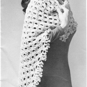 Może przedstawiać: Biały szal wykonany na szydełku z delikatnym wzorem ażurowym. Szal jest zarzucony na ramiona osoby w czarnej sukience.