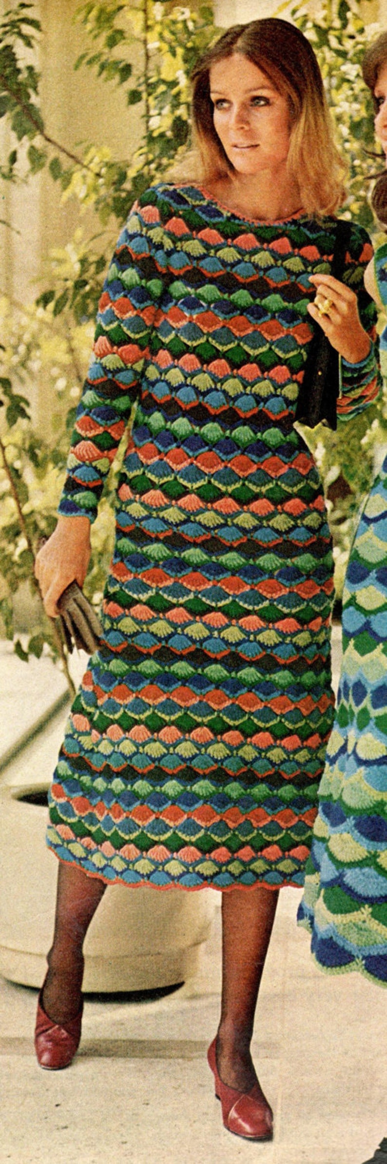 May include: A woman wearing a long-sleeved, multi-colored crochet dress with a geometric pattern. The dress has a scalloped hem and is paired with red shoes.