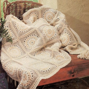 May include: A crocheted throw blanket with a beige and cream color scheme. The blanket is made of squares with a circular pattern in the center of each square.