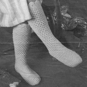 May include: A pair of crocheted leg warmers in a light beige color. The leg warmers are made with a simple stitch pattern and are long enough to cover the entire leg.