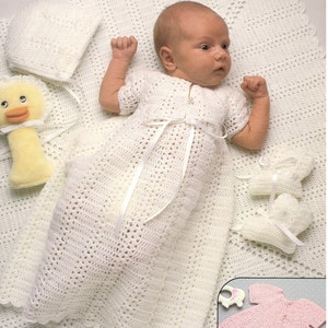 May include: A white crocheted baby gown with a white satin ribbon tie, a white crocheted bonnet, and a white crocheted blanket. The baby is wearing the gown and lying on the blanket.