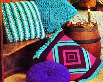 May include: Four crocheted cushions in various colors and patterns, including turquoise, white, pink, and purple. The cushions are arranged on a wooden shelf and a wooden barrel.