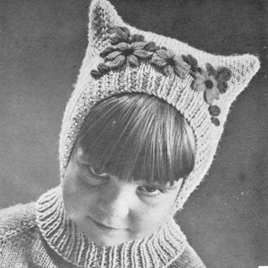 May include: A knitted hat with cat ears and flower embellishments. The hat is white and the flowers are a light brown color.