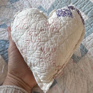 May include: A white heart-shaped pillow with a quilted design and pink and purple fabric accents.