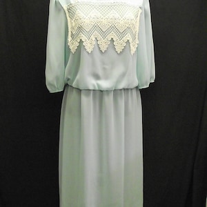 Può includere: Un abito azzurro chiaro con un collo in pizzo bianco. L'abito ha una vita a pieghe e una gonna fluida.