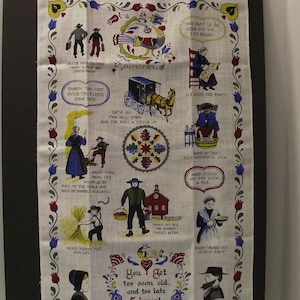 May include: A white tea towel with a colorful folk art design featuring various scenes of Amish life. The text "You get too soon old, and too late Schmart" is printed in the center of the towel.
