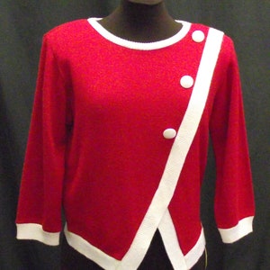 May include: A red sweater with white trim and three white buttons. The sweater has a diagonal white stripe down the front.