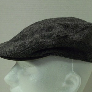 May include: A gray herringbone tweed newsboy cap with a black leather brim.