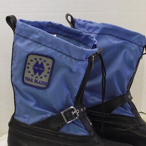 May include: A pair of blue and black winter boots with a zip and buckle fastening. The boots have a Trail Blazer logo on the side.
