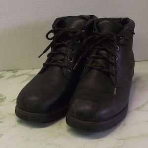 Puede incluir: Un par de botas de cuero negro con cordones y tacón bajo.