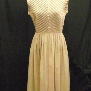 May include: A sleeveless, white dress with a pleated skirt and a button-up front. The dress has a V-shaped neckline and a fitted bodice.