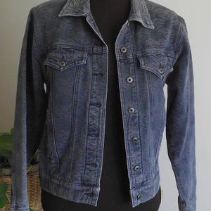 May include: A blue denim jacket with a textured pattern. The jacket has a button closure and two front pockets.