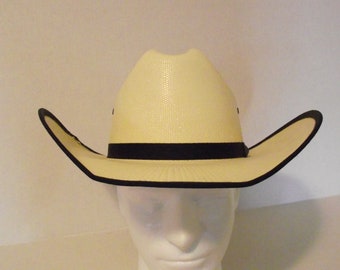 Puede incluir: Un sombrero de vaquero de paja con corona y ala de color crema, con una banda y ribete negros. El sombrero tiene un diseño occidental clásico, con un ala ligeramente curvada y una forma estructurada.